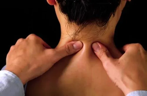 Two thumbs pressing into both sides of the nape, just below the hairline — an acupressure technique working directly on the tight muscle points of the neck and shoulder